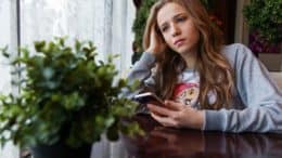 ung-kvinde-sidder-ved-et-bord-med-sin-mobiltelefon-og-keder-sig-kedsomhed